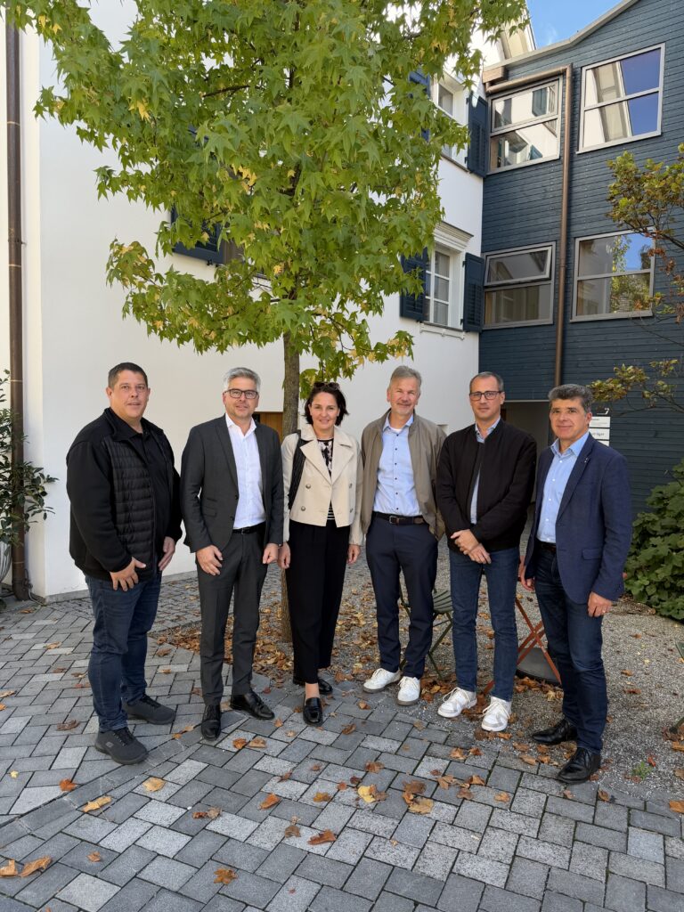 Sechs Personen stehen vor einem Gebäude mit Bäumen und Herbstlaub in Österreich.